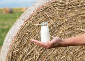 a man holds a jar of fresh milk in his hand on the background of a field with hay