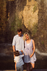 Fototapeta premium The young pregnant family is standing on the rock background
