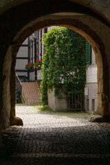 Fototapeta premium dark medieval archway leads into daylight with truss house and cobble stone street of town, Tecklenburg, Germany