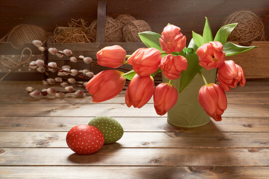 Bunch of red tulips, Easter eggs and pussy willow twigs. Springtime decorations on rustic wooden background. Retro toned image of Easter decorations.in low key. Sunlight with shadows.