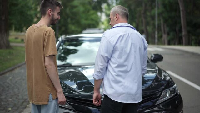 Positive Middle Aged And Young Caucasian Men Closing Car Hood And Giving High-five. Happy Father And Son Repairing Broken Automobile On Summer Road Outdoors. Lifestyle And Joy Concept.