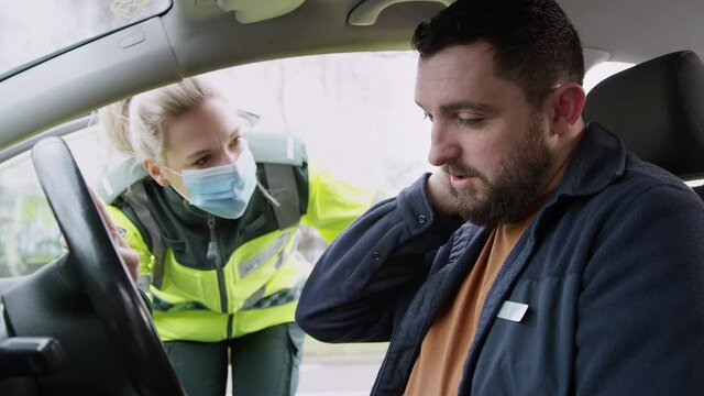 Female paramedic medic wearing face mask assessing whiplash neck injuries to male driver inside car involved in road traffic accident - shot in slow motion