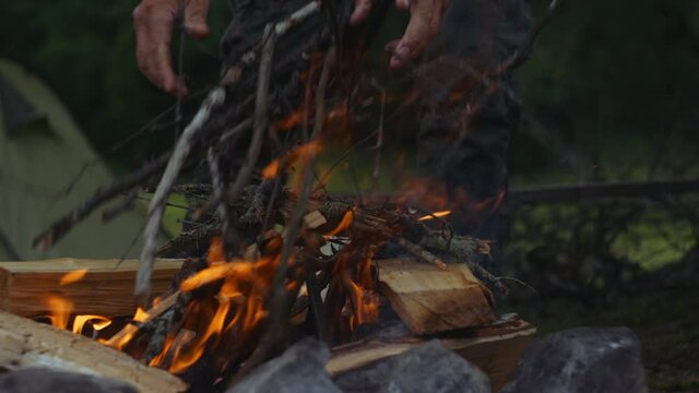 campfire in the camp of tourists. a person keeps the fire burning , a person throws branches into the fire. slow motion