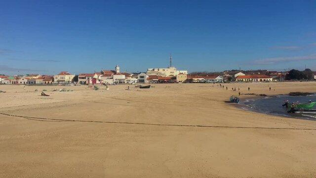 View of people walking on the beach, traditional fishing boat and restaurants at Aguda beach. Vila Nova de Gaia, Porto, Portugal