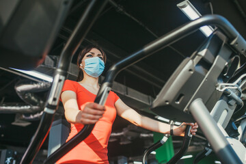 Fototapeta na wymiar An active woman in a protective medical mask training in gym, during COVID-19 epidemic. Sport and quarantine.