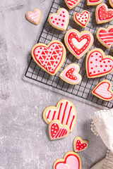 assortment of homemade heart shaped valentines sugar cookies with red, pink, and white icing designs cooling on a wire rack