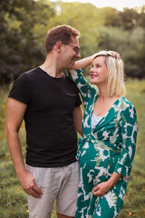 Portrait of the smiling pregnant couple  who is standing in the garden and looking at each other
