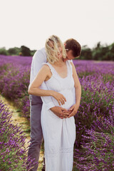 The happy young man hugging and kissing his smiling pregnant wife in the lavender field