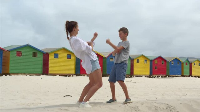 A girl with boy dancing on the white sands of South Africa near the colorful wood Muizenberg Beach Houses.