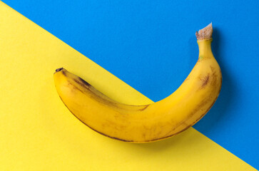 A banana lying on blue and yellow background