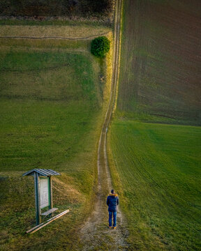 Droneception image showing a man watching along a long way between the field to a tree at the curved horizon.