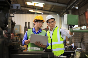 Asian engineering manager and mechanic worker in safety hard hat and reflective cloth using lathe machine inside the factory