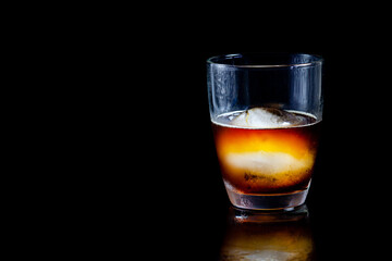 ice ball in glass of whisky on a reflective black table.