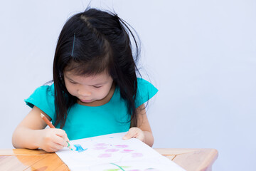 A 3-4 years old Asian pupil girl does art and paint wood with two color pencil crayon. Cute children learn at home. Preschoolers enjoy art. Isolated white wall background.