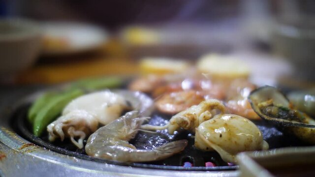 Close up shot of vegetable, shrimps and cuttlefishes being cooked and grilled.