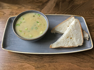 An artisan vegetable soup, featuring sweet potato, apple, leek, and celery is shown alongside two slices of white bread, plated on a table in a cafe.