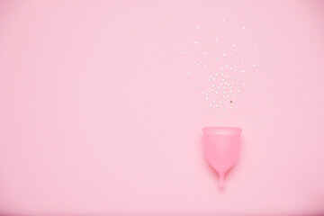 Menstrual cup with glitter on pink background. Alternative feminine hygiene product during the period. Women health concept
