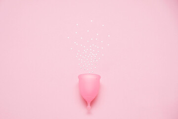 Menstrual cup with glitter on pink background. Alternative feminine hygiene product during the period. Women health concept