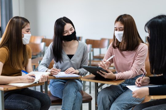Group of diverse international students wearing protective  masks and talking, discussing project, sitting at desk in the classroom at the university
