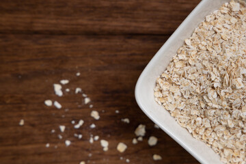 Oatmeal flakes in a wooden bowl on a white background.