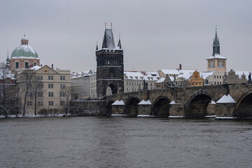 panoramic view of the snow-covered Charles Bridge on the Vltava River and snow on the roofs of buildings and towers in the center of the old town of Prague
