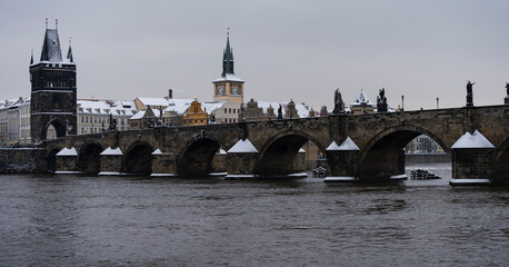 Fototapeta premium panoramic view of the snow-covered Charles Bridge on the Vltava River and snow on the roofs of buildings and towers in the center of the old town of Prague