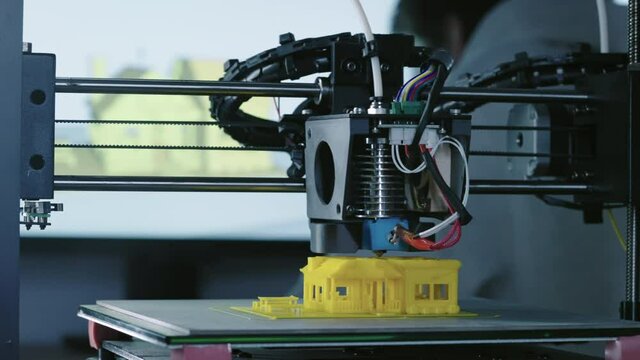 Timelapse of 3d Printer printing yellow small house with engineer constructor in background at pc model shot in 4k