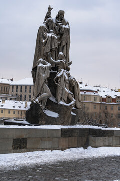 view of snow-covered statues and street lights on the old stones of Charles Bridge on the Vltava River and in the background the snow-covered roofs of buildings