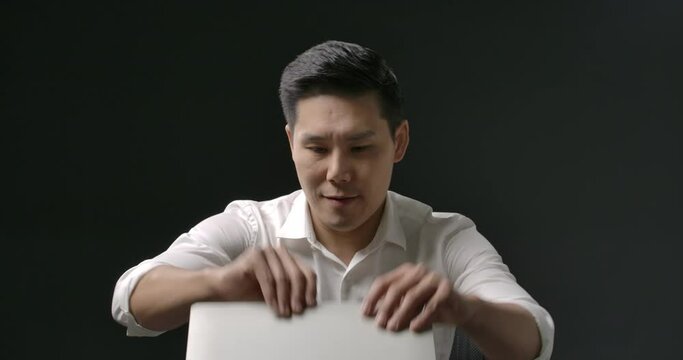 Young glasses asian man using laptop computer for work or study online. Handsome guy in white shirt at house during quarantine. Social distance new normal concept.