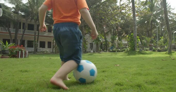 Child play football on a summer day. Happy kid play ball outdoor lifestyle sports in park healthy. Baby son playing football soccer in the park on the grass.
