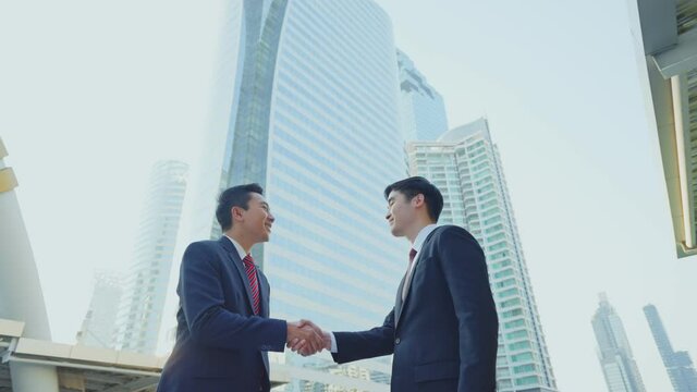 Asian businessmen making handshake in the city, skyscraper background.