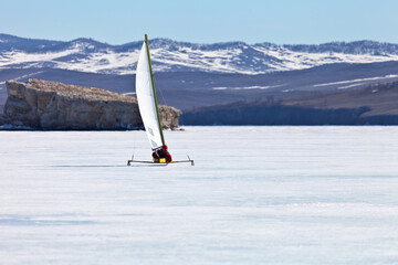 Baikal Lake. A tourist travels under a sail on a ice-skating ice boat - boeier across frozen Small...