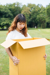 Young asian thai woman hipster curly hairstyle on white dress holding big huge cardboard box. Gift box. Looking inside with surprise expression.