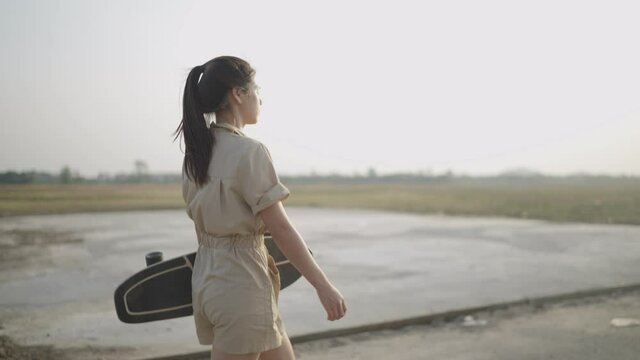 4k Video slow-motion, Asian women carry a surf skateboard out to the streets outside the country road with mountain views in the evening. lifestyle concept.