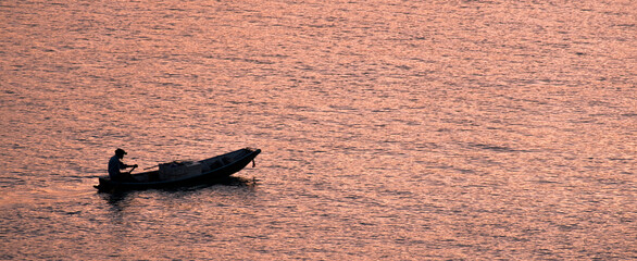 Shadows of the fishermen paddle back to the shore in the evening when the sun's rays reflect the glittering surface.