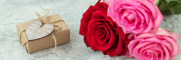 Banner of romantic gift for valentine's day with space for text.Gift wrapped in craft paper next to bouquet of roses on white stone background. Marriage proposal concept.