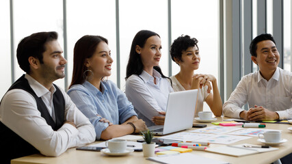 Group of five diversity businessmen, two men and three women sitting at meeting desk and pay attention for speaker of the conference.