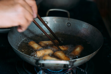 Deep frying spring rolls in a pot on the stove using chopsticks.