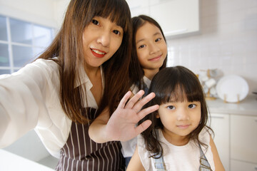 Cute and beautiful mother with two young and little daughters, 3 years and 7 years old, taking a selfie photo with a smartphone in modern kitchen. Concept love and relationship of family