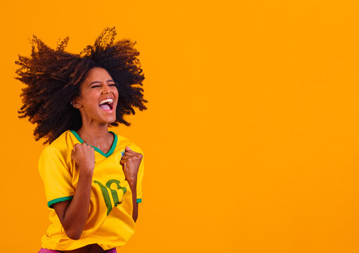 Brazilian supporter. Brazilian woman fan celebrating on soccer or football match on yellow background. Brazil colors.