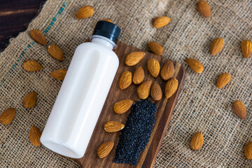 Top view of almond milk with sesame in a plastic bottle with almonds nut and sesame seeds on rustic fabric wooden tray and table. Concept of organic healthy detox and diet food and drinks.