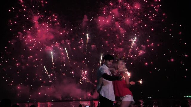 Happy young couple enjoying fireworks display dance and hug.