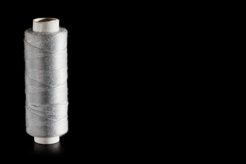 Reel with gray sewing silk threads isolated on a black background, close-up, copyspace. Bright background for sewing and needlework