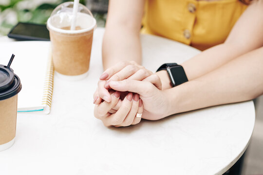 Hands of young couple in love sitting at table in outdoor cafe and touching hands