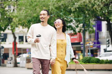 Happy beautiful young Chinese couple holding hands when walking on city streets