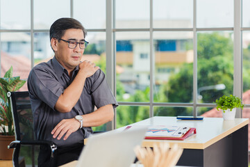 Asian hard senior businessman working with laptop computer has a problem with shoulder pain. Old man feeling pain after sitting at desk long time, Healthcare and medicine office syndrome concept