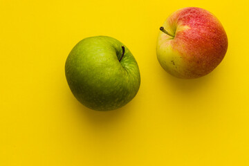 Green apple and yellow-red apple on a yellow background