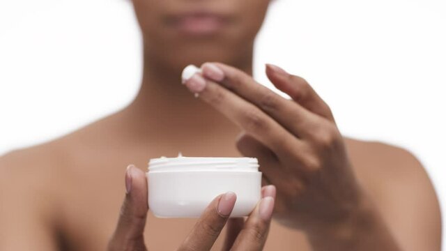 Organic cosmetics. Close up of blurred african american lady taking cream and applying it on face, focus on jar