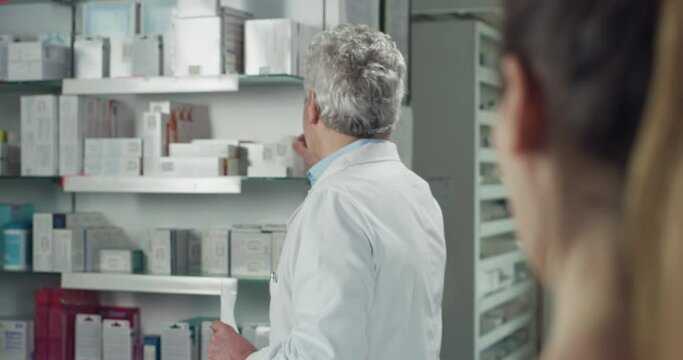 Cinematic shot of smiling male professional pharmacist consultant is handing over prescribed medicines to patient in pharmacy. Concept of drug store, medicine, health care, apothecary, assistance.