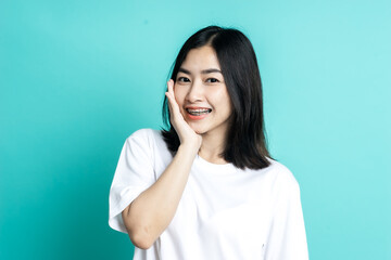 Fototapeta premium Asian woman wearing dental braces pointing to tooth sample and smiling with her healthy white teeth isolated shot on blue background